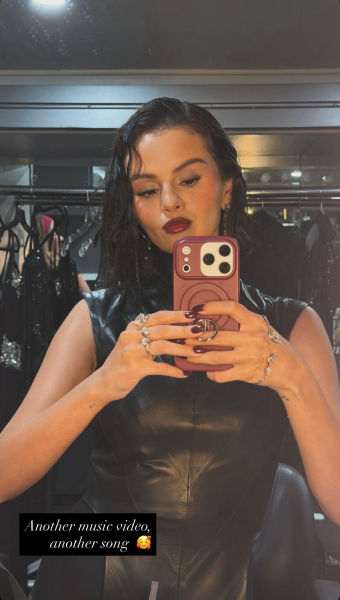 Selena Gomez poses in the mirror wearing a black leather dress burgundy nails and lips and waves.